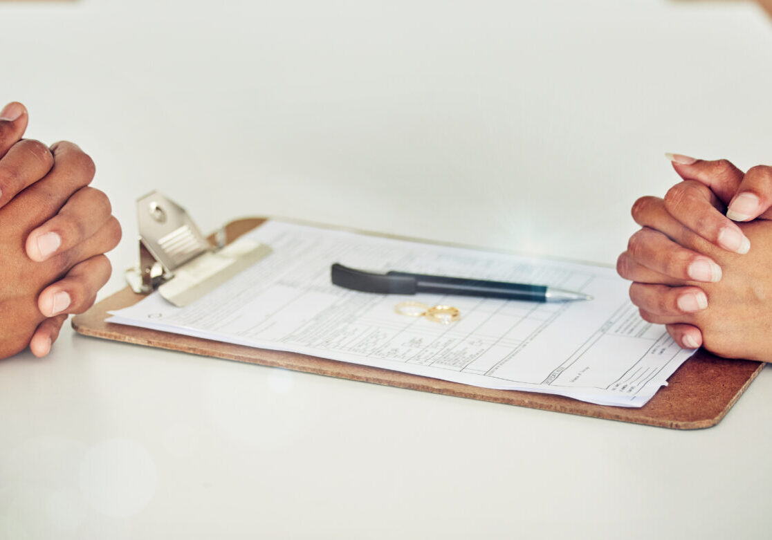 Couple hand sign legal divorce documents, contract or paper deal in a lawyer office with ring placed on table. Woman and man with signature on marriage paperwork after agreement at family law office